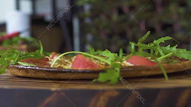 Fresh herbs falling on hot italian pizza slow motion. Close up pizza with fresh herbs in pizzeria. Food seasoning