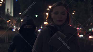 Female bandit in mask and hood stealing woman handbag on dark city street, crime