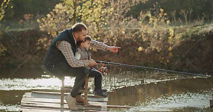 Beautiful autumn day dad with his son spending a wonderful time together catching some fish from the lake.