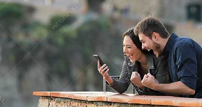 Excited couple checking phone content in a balcony