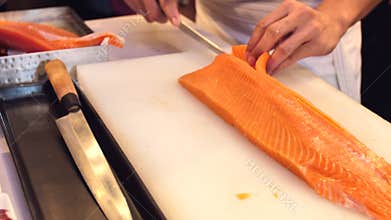 Close-up of sushi chef show one`s capability slices fresh salmon at sushi bar.