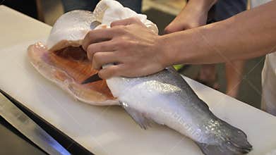 Close-up of sushi chef show one`s capability slices fresh salmon at sushi bar.