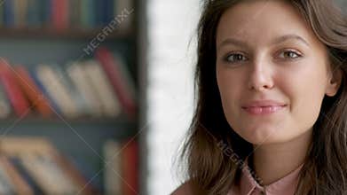 Close up portrait of young pretty librarian woman smiling happy looking at camera in library bookshelf background