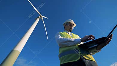 Energetics expert is navigating his computer while standing near a windmill. Renewable alternative energy, environment