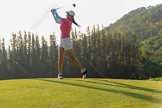 Asian woman golf player doing golf swing tee off on the green evening time, she presumably does exercise.