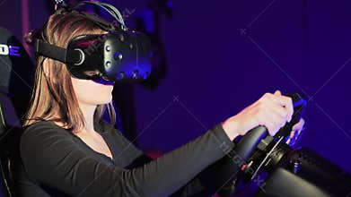 Young woman playing in car drive simulator at VR club, using modern virtual reality headset. Video game concept