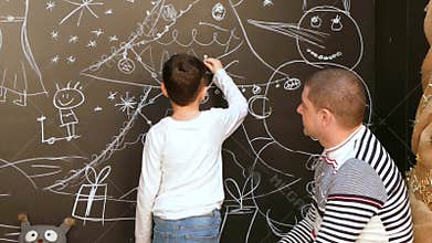 Boy with father paints a picture on the wall with chalk on a Christmas theme