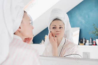 Young woman looking at camera and applying cream on face