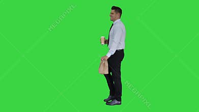 Businessman walking with take away coffee and paper bag with lunch on a green screen, chroma key.