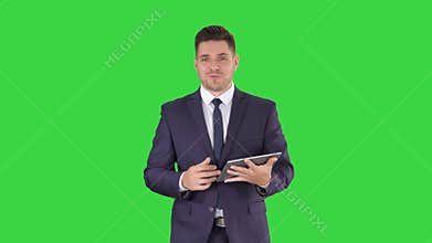 Businessman swiping pages on a tablet and talking to camera explaining something while walking on a Green Screen, Chroma