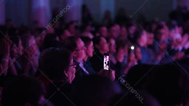 A woman recording the jazz performance on her phone. The audience clapping their hands