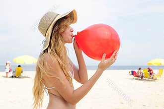 Woman inflating a red balloon on the beach