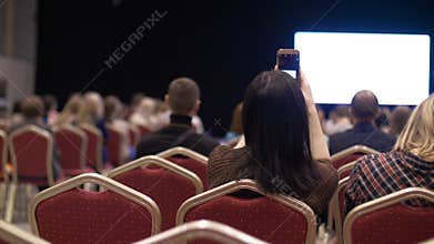 People listen to the presentation the conference hall. Back view. Empty chairs