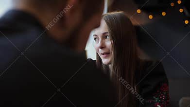 Close up portrait of happy young girl is drinking coffee, talking and smiling with her boyfriend while sitting at the