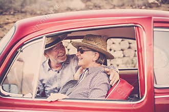 Nice beautiful couple of senior adult people inside an old red vintage car enjoy and stay together in outdoor travel leisure