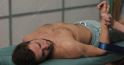 Physiotherapist doing healing treatment on man`s arm with blue elastic band. Alternative medicine treatment and