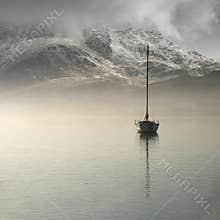 Stunning landscape image of sailing yacht sitting still in calm lake water with mountain looming in background during Autumn Fall