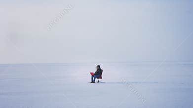 Wide shot of alone businessman in warm coat and hood sitting in snow desert and working with laptop attentively.