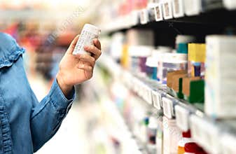 Customer in pharmacy holding medicine bottle. Woman reading the label text about medical information or side effects in drug store