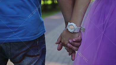 A guy with a girl walking in the Park holding hands. Young lovers walk. Close-up of their hands. Rear view.