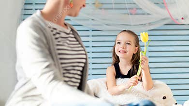 Cute young girl giving her mom a flower. Family celebration concept. Happy Mother`s Day or Birthday Background.