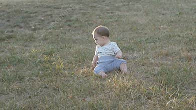 Small baby girl sitting on grass in park. Beautiful baby portrait in nature