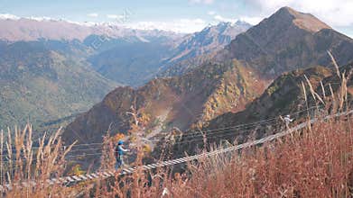 Girls in helmets walking along hanging rope bridge over abyss