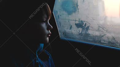 Atmospheric shot of little 4-6 year old thoughful Caucasian boy looking out of foggy car window in dusk dark evening.