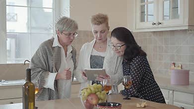 Woman showing to her friends photos on tablet. Group of three mature women communicating chatting spending time in
