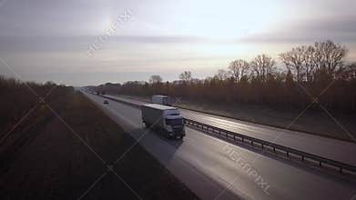 AERIAL: Delivery trucks driving towards the sun. the car with the container rides on the road to the sunset. Truck rides