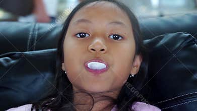Little girl eating bubble gum on sofa