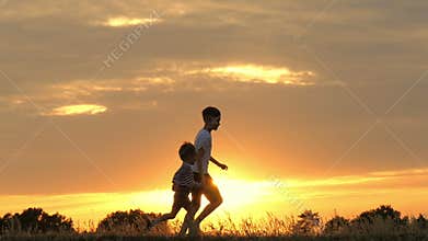 Two happy children running after each other against the sunset. The two brothers are playing catch-up in a slow motion