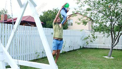 Dad with a four-year-old son playing ball, football, in the yard on a green lawn, in the summer.