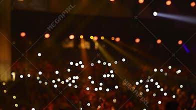 Audience is shining with flashlights of phones.