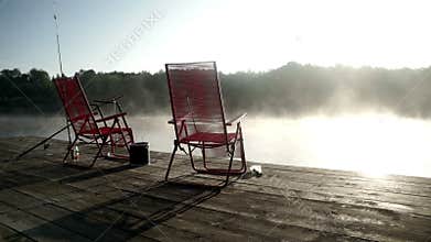 Fishing chairs standing at fishing pier on background morning fog over water
