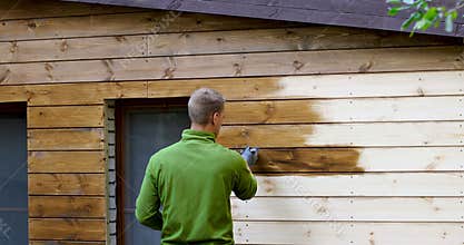 Painter with paintbrush painting house facade with wood protective color