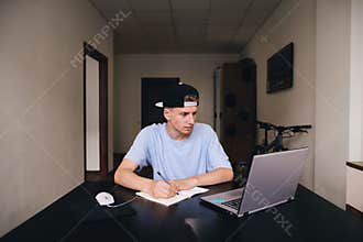 Student studies at home. The teenager looks at the computer and writes the text to the notebook.