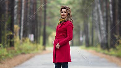 Portrait of a young woman in an autumn park. Beautiful girl in red coat posing and smiling at the camera