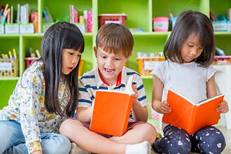 Children sitting on floor and reading tale book in preschool li
