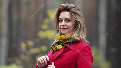 Close-up portrait of a beautiful young woman on a background of autumn forest. Girl in red coat smiles and looks at