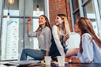 Happy female teenagers sitting on table looking and pointing at stylish light bulbs and relaxing during a recess between