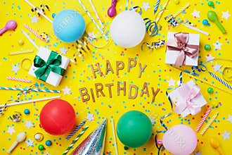 Happy birthday background or greeting flyer. Colorful holiday supplies on yellow table top view. Flat lay style.