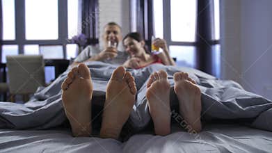 Close-up bare feet of young couple under blanket