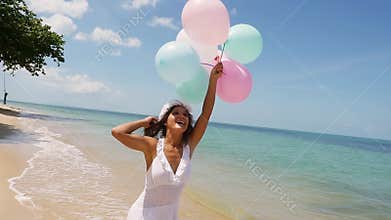 Joyful pretty girl in white dress running on the beach jumping holding balloons in hand. slow motion. Concept happiness
