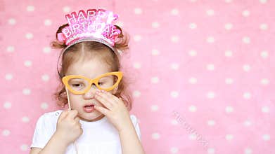 Funny happy child celebrate birthday, have fun, laugh. Close-up portrait cute girl on pink background. Decor and