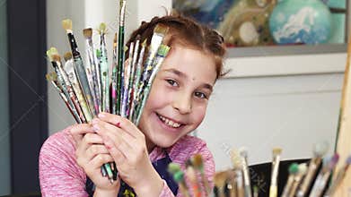 Cute happy girl smiling to the camera holding bunch of paintbrushes