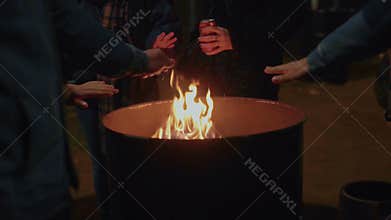 People warm hands next to fire on street