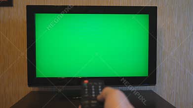 Male hand using a remote control to flipping channels on green screen TV. Arm of man surfing television channels with