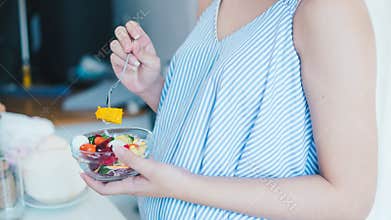 Asian pregnant woman is eating salad. She looks healthy. Because the food is beneficial.