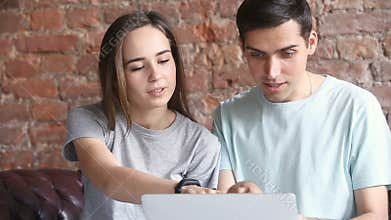 Young casual couple using laptop, choosing goods in online shop